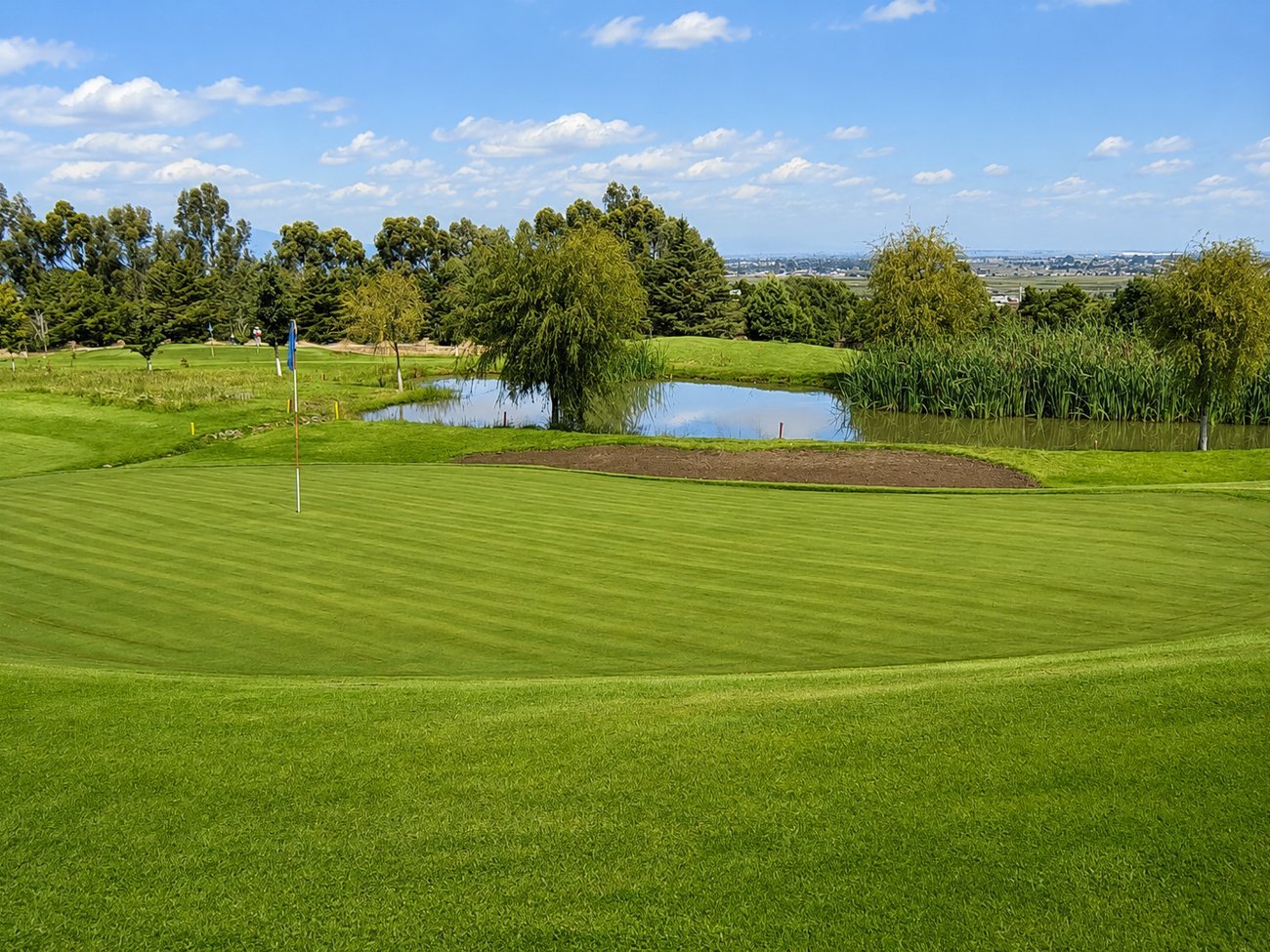 Green del campo de golf junto a un lago con reflejos